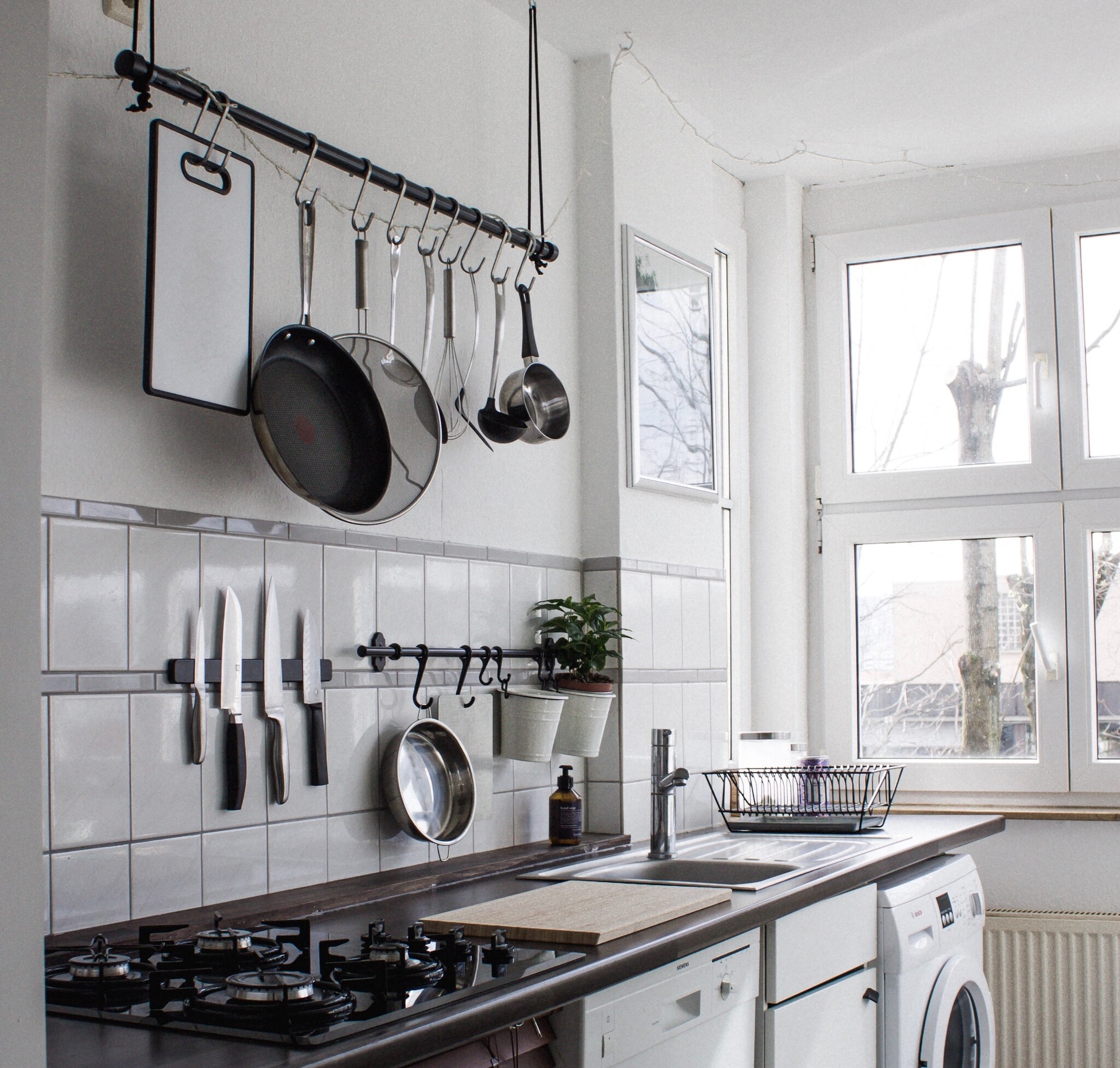 A kitchen with white appliances; black countertops; and pots, pans, and knives hung on the wall. 