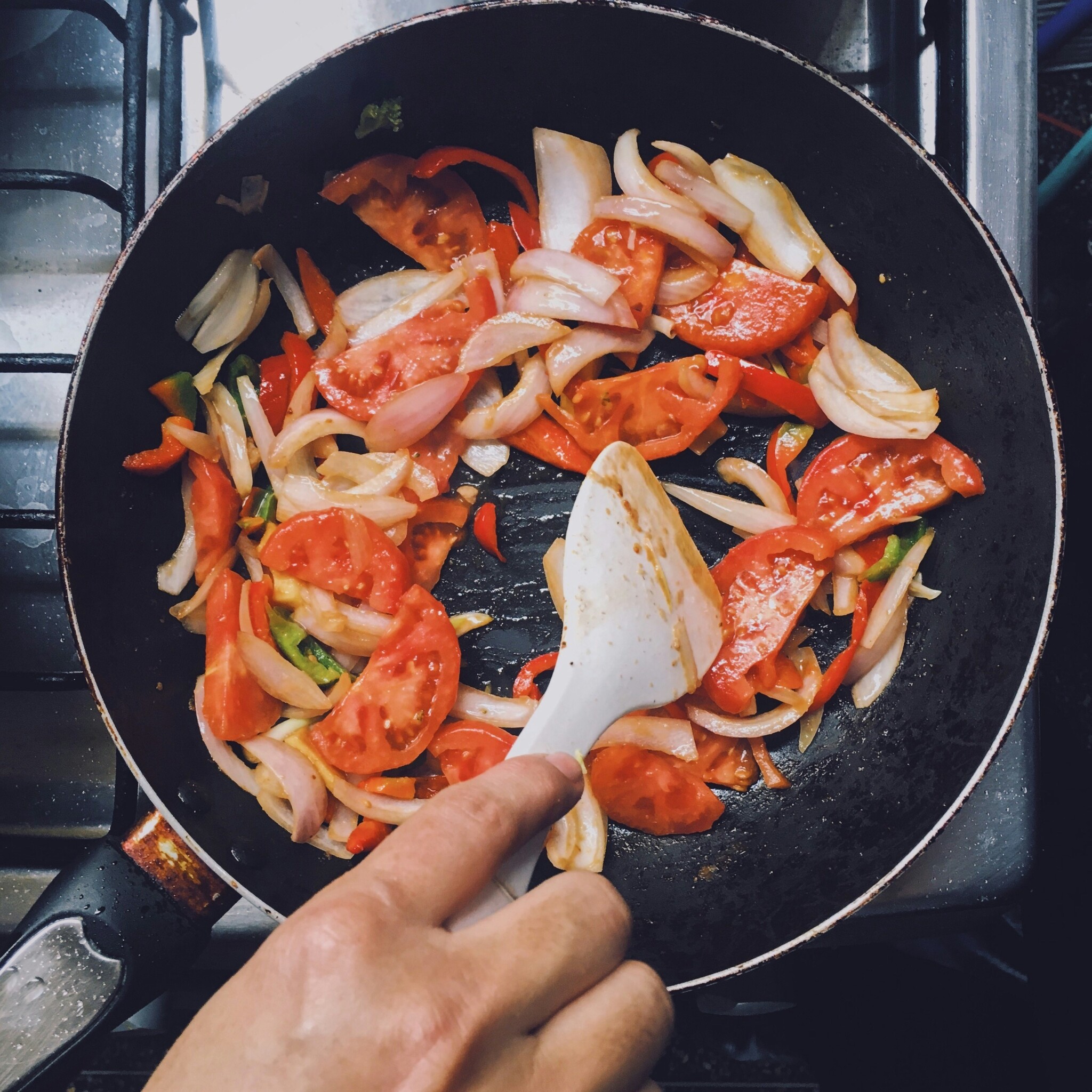 Tomatoes, white onions, and green peppers being sauteed in a skillet