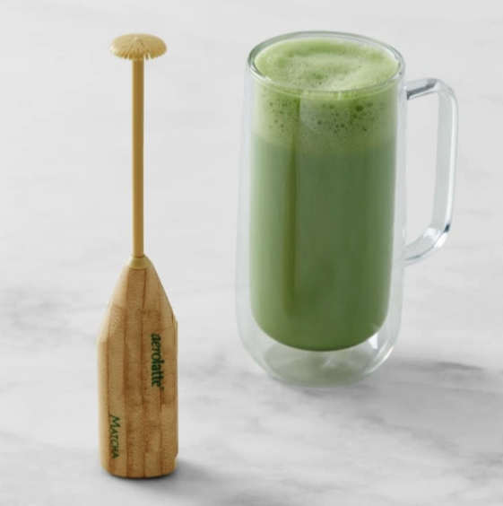 Aerolatte matcha frother sits on a white marble surface next to a clear mug of frothed matcha. 