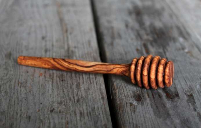 Natural olive wood honey dipper sits on a grey wooden surface. 