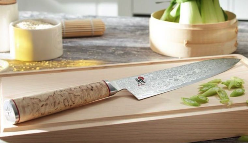 Miyabi Birchwood knife sits on a cutting board with sliced green onions