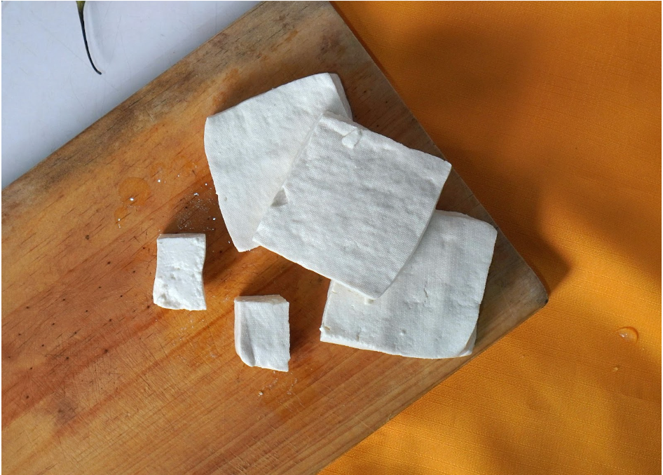 Blocks of tofu sit on a wooden cutting board. 