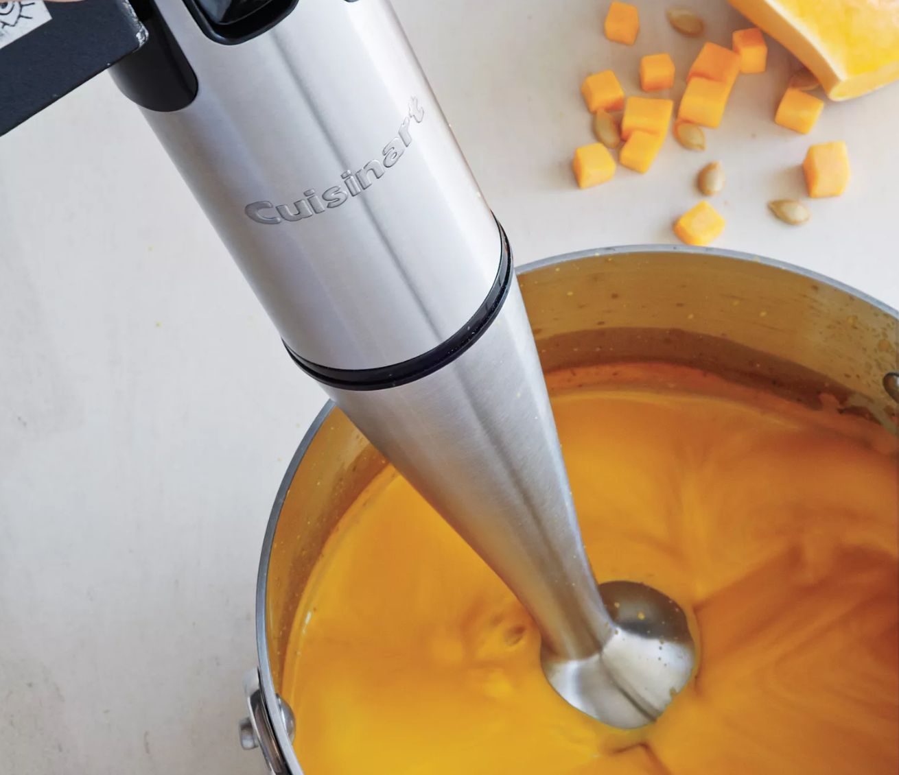 A cuisinart immersion blender blends a squash pureé in a stock pot with cubed pieces of squash beside it. 