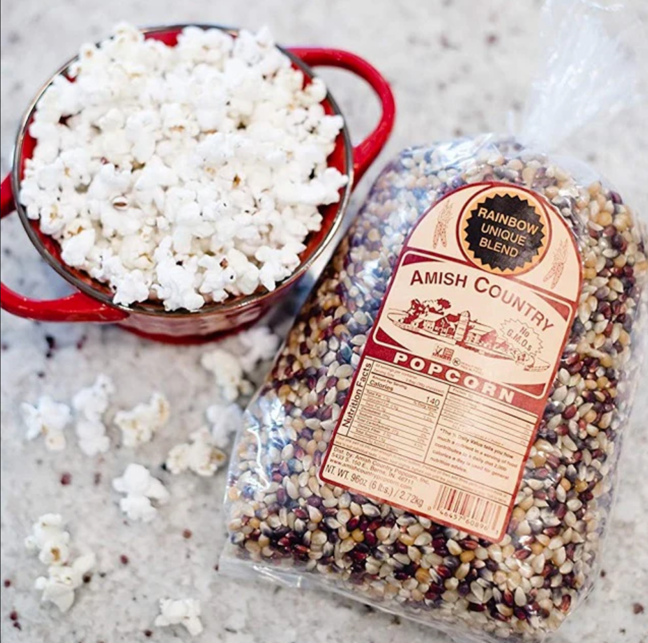 a small, red dish filled with freshly popped popcorn sits beside a bag of Amish Country popcorn kernels on a granite countertop. 