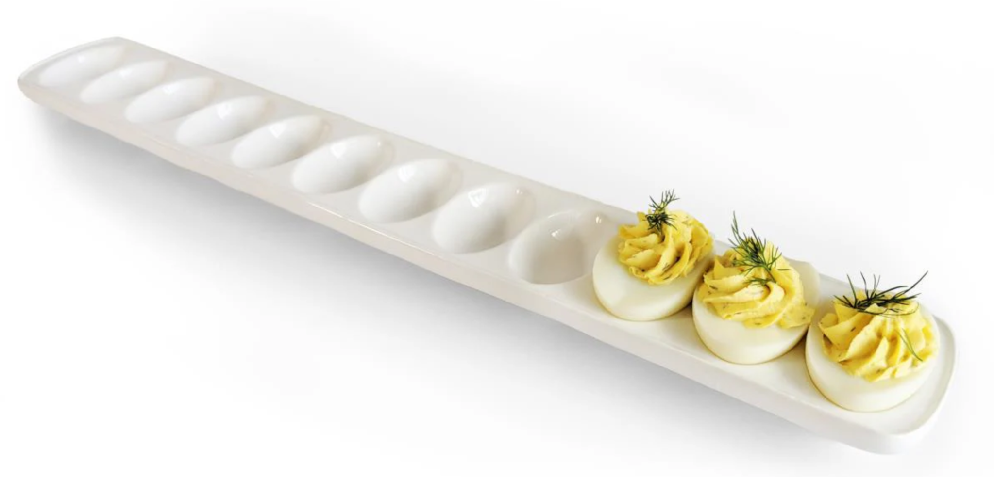 A long, white deviled egg serving tray with three deviled eggs inside of it.