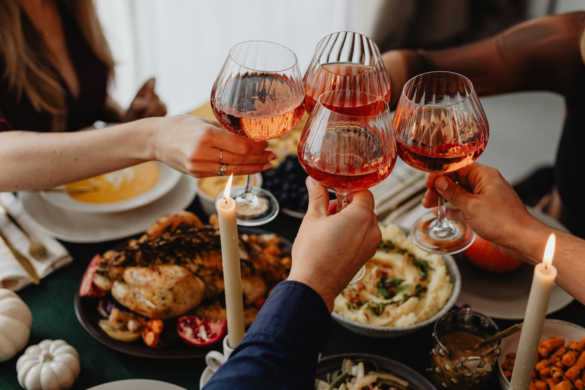 a group of four people toast with glasses of red liquid over a table laid out with a Thanksgiving spread of roasted turkey, mashed potatoes, vegetables, and soup. 