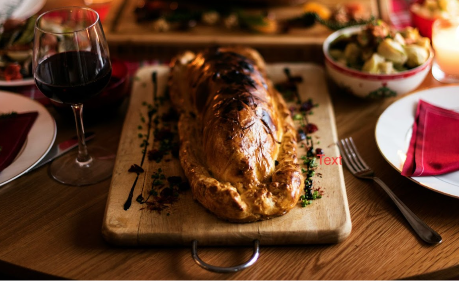 A mushroom Wellington sits on a cutting board on a wooden table surrounded by other dishes and a glass of red wine. 