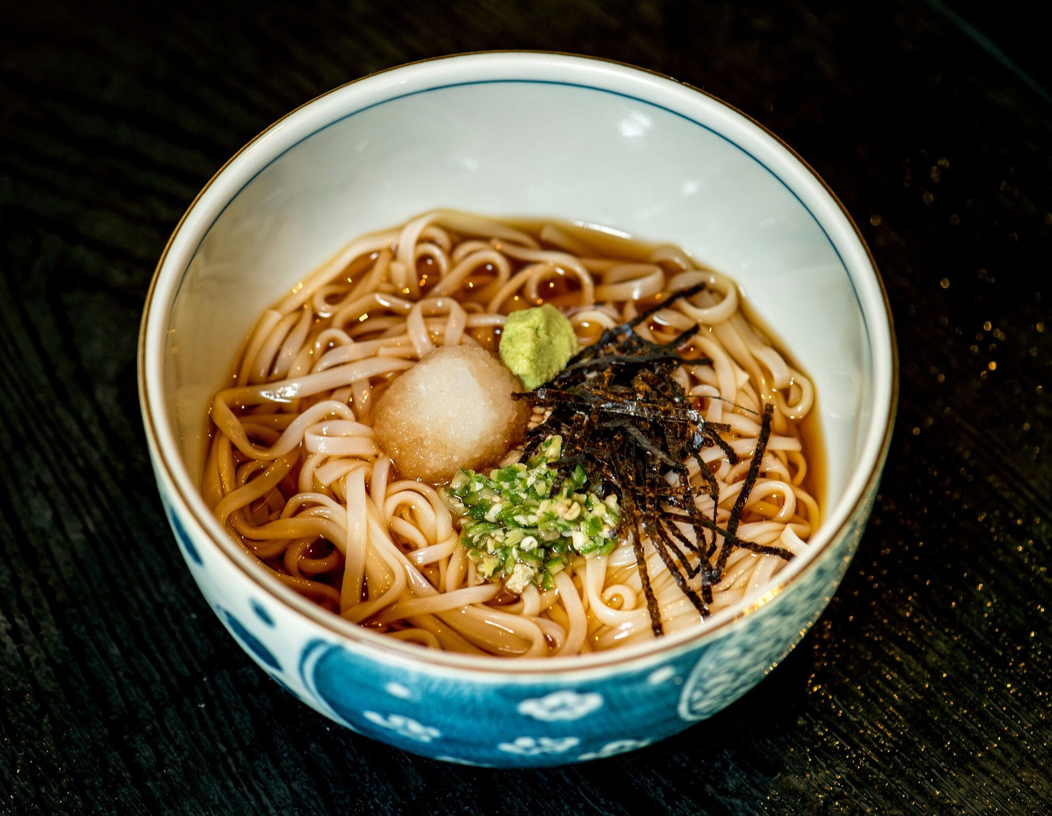 Toshikoshi soba noodles sit in a decorative blue bowl on a black tabletop. 