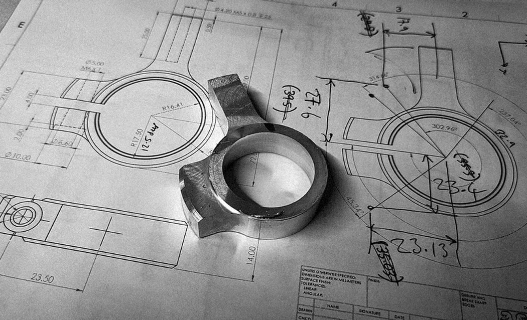 Black and white photo of a machined drop out on top of a bicycle frame's blueprint.