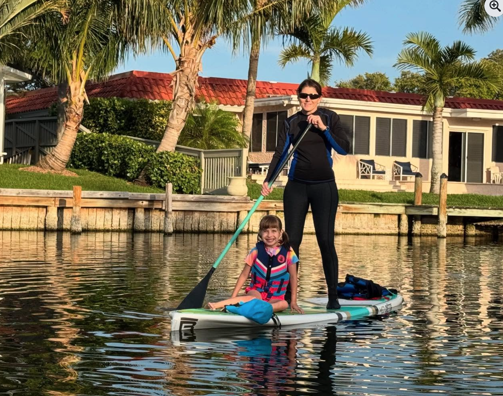 Family paddle boarding together in calm lagoon water with child sitting on board in front