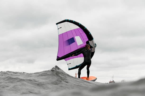 Wing foiler with purple wing practicing on ocean swell under cloudy skies