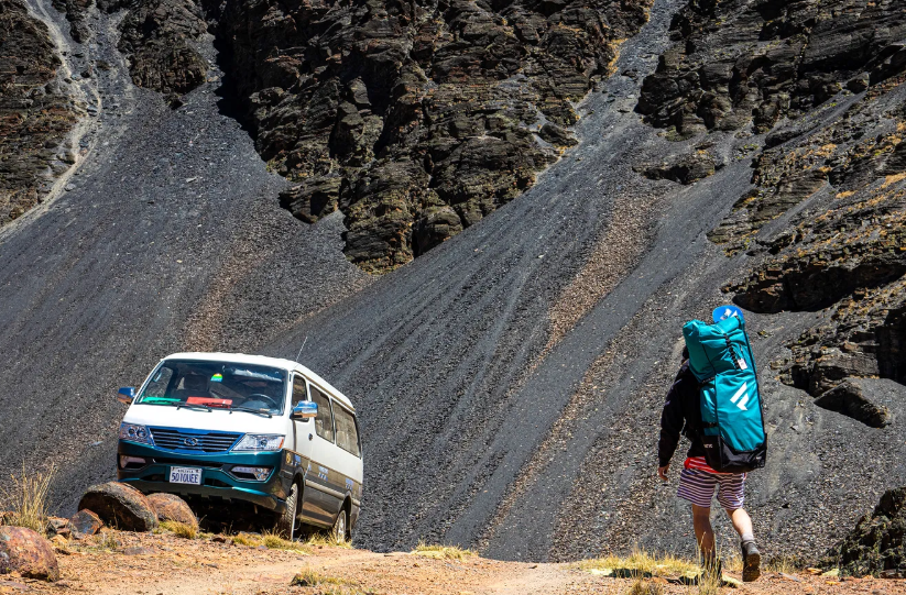 Paddler hiking with the packed Fanatic Fly Air Pocket Edition SUP bag in the mountains, illustrating easy transport on trips and adventures.