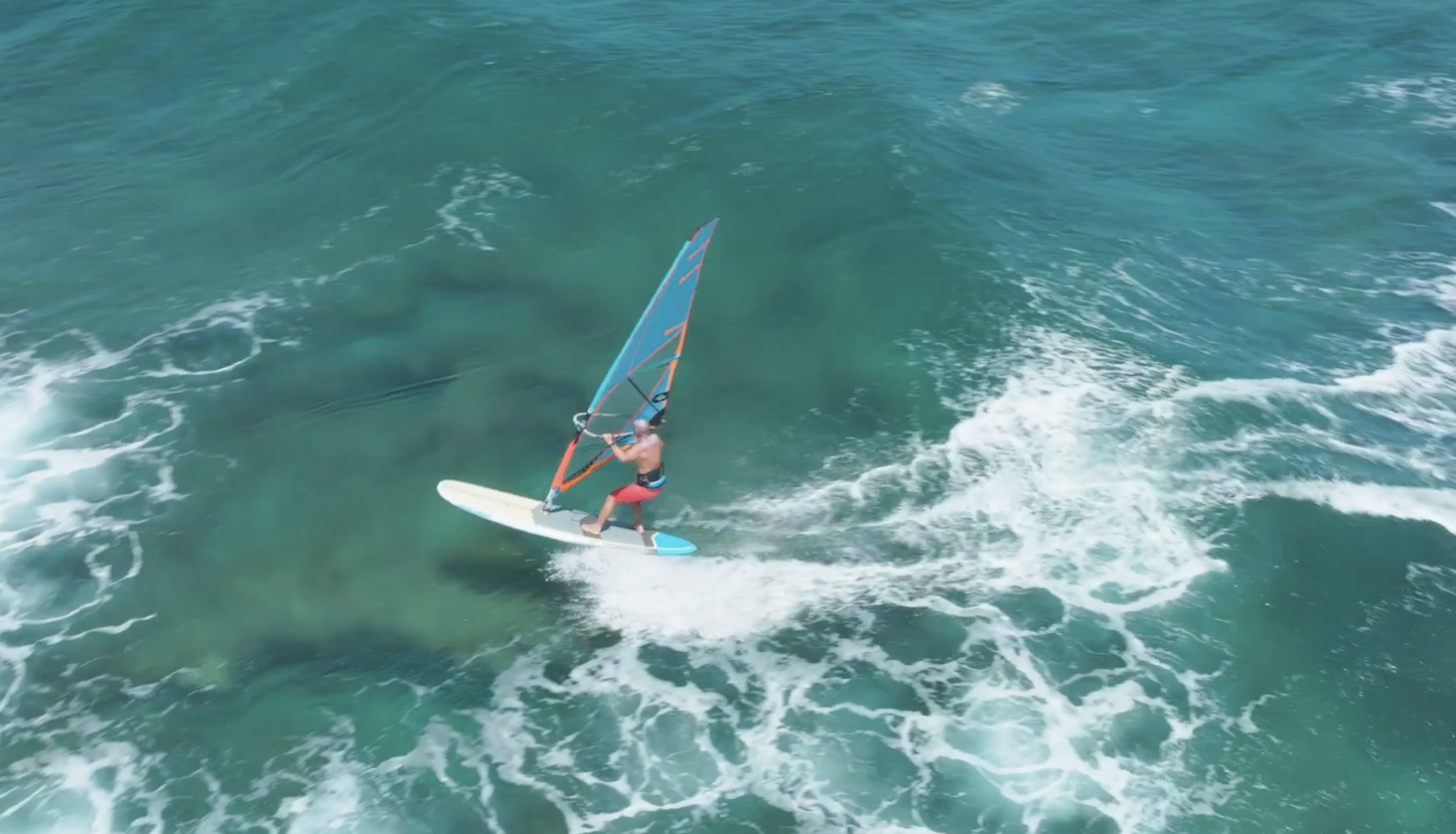 A rider windsurfing on a Naish Nalu GTW board over clear turquoise water