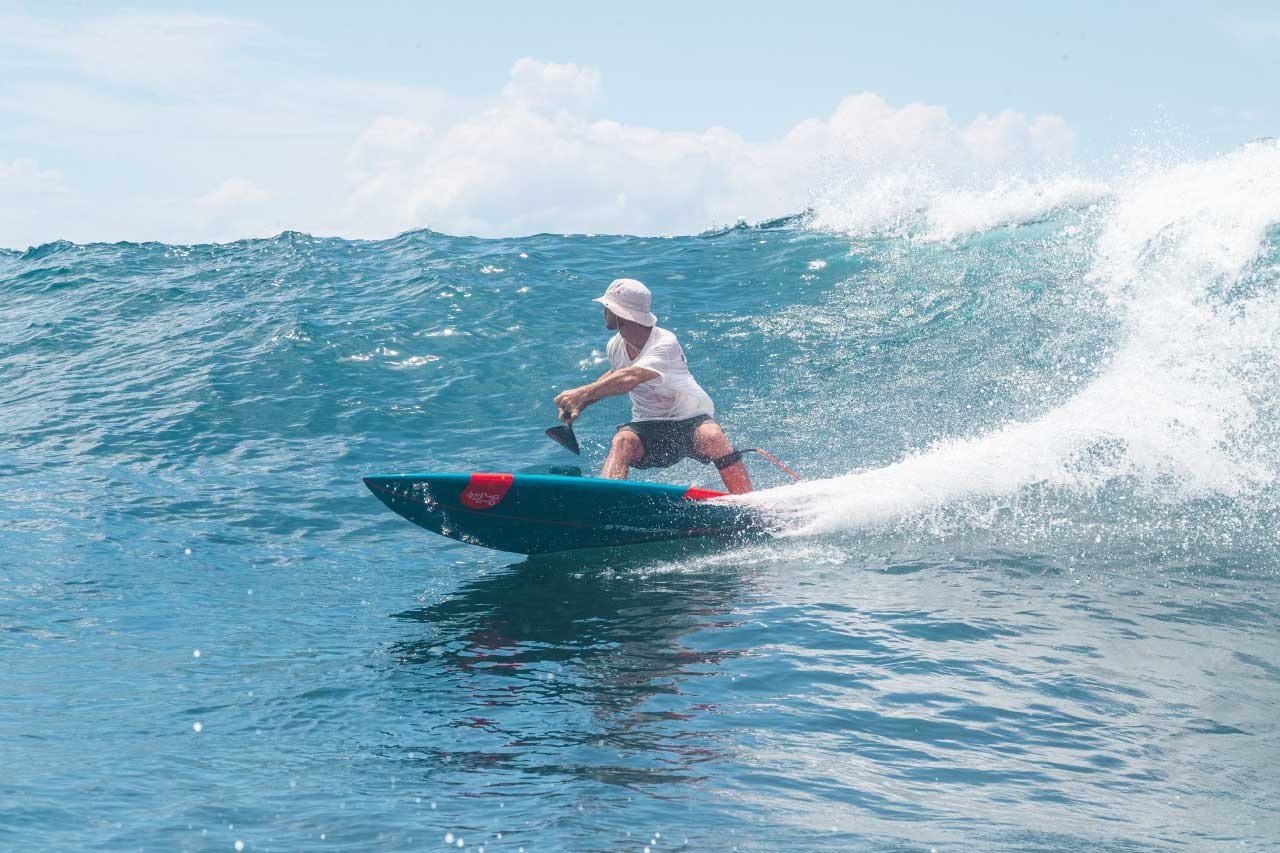 Starboard Pro surf SUP rider carving on a clean blue wave in tropical conditions