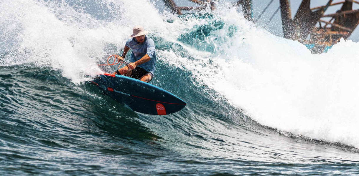 Adult rider carving a Starboard Pro SUP under the pier in powerful surf