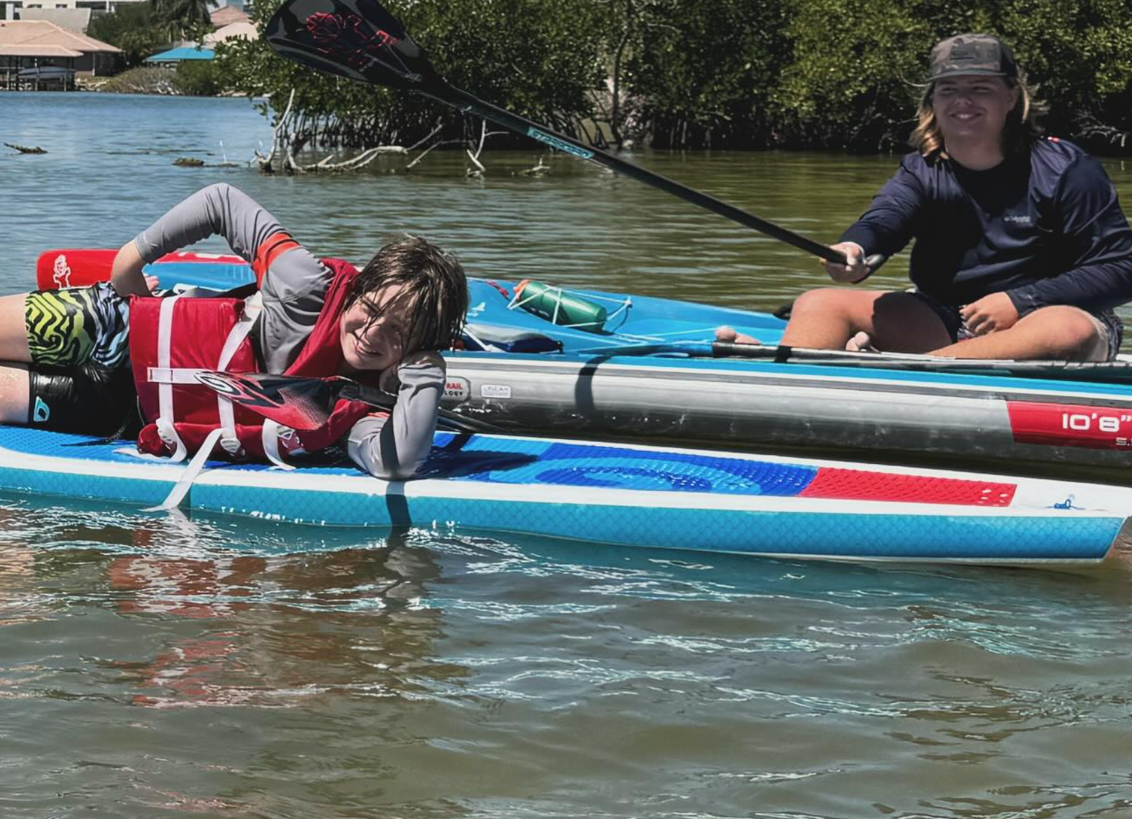 Two kids on a paddle board having fun.