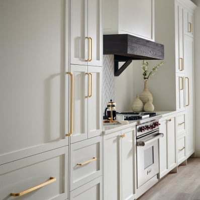 Open kitchen with white cabinetry and large gold handles. A dark wood range hood above a stove.