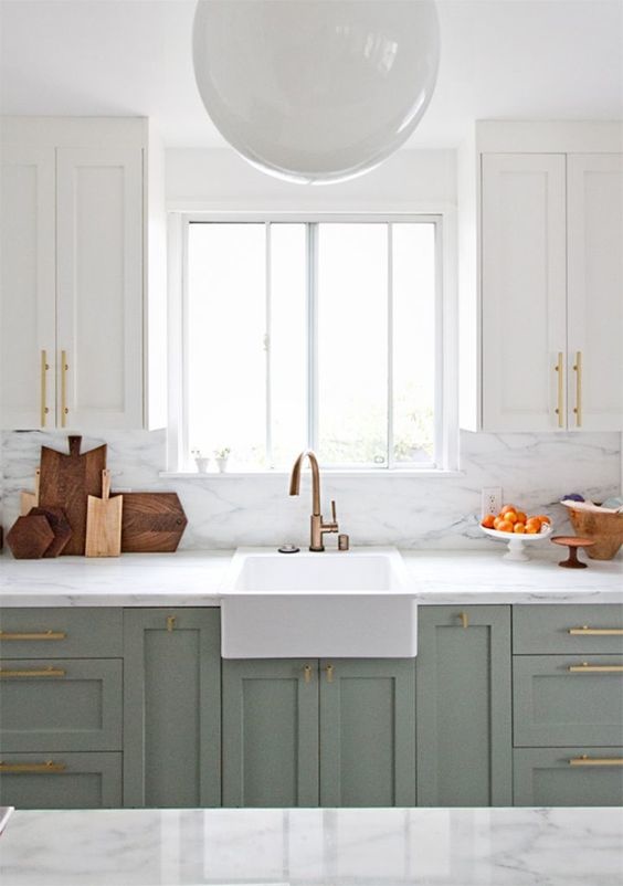 Light green cabinetry with gold handles and a large farmhouse sink.