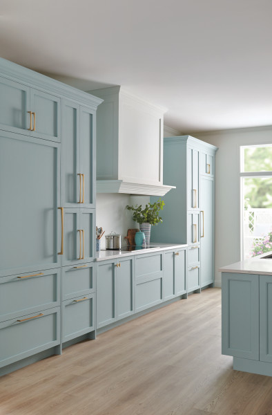 Light blue kitchen cabinets with bright gold handles and a wood range hood. Large bright kitchen.