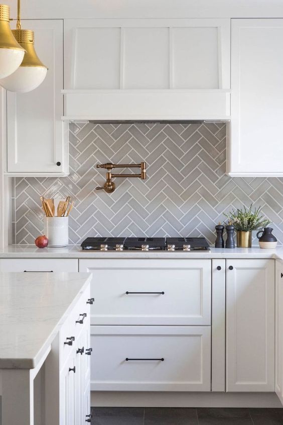 Chevron patterned grey backsplash with white cabinets and a decorative white range hood. 