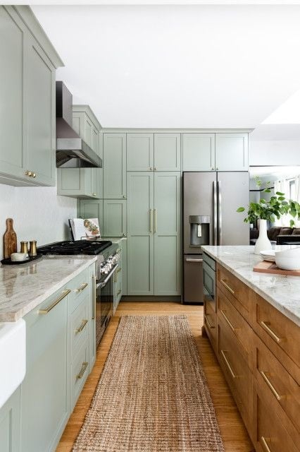 Light green cabinetry in the surrounding kitchen with a wood island in the middle.
