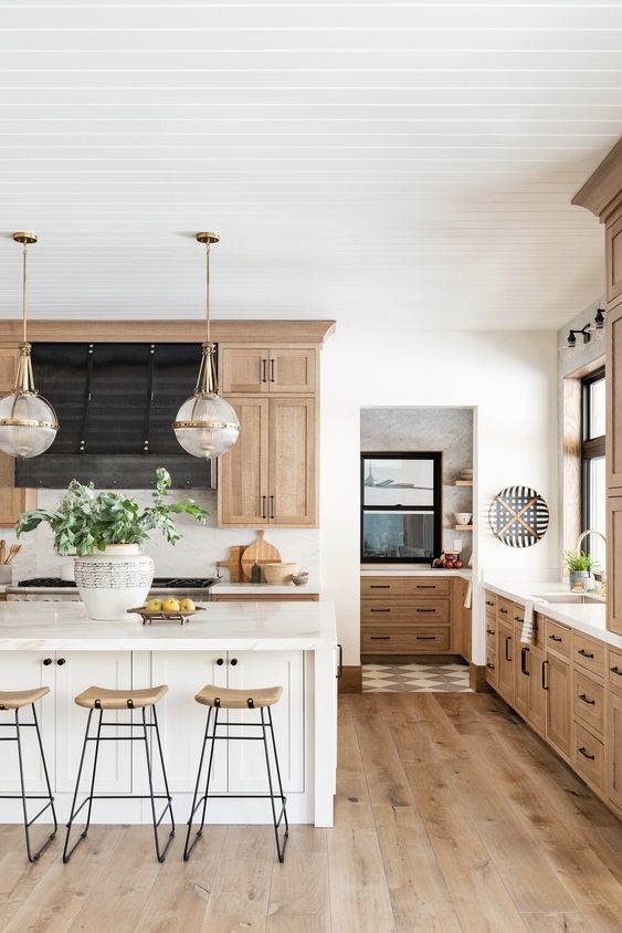 Mix of wood and white cabinetry in a large open kitchen. Three stools sit at a large island.