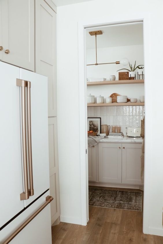 Walk in pantry with counter tops and a double door white fridge with gold appliance pulls.