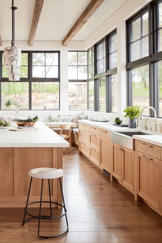 Natural wood cabinetry with white countertops and room is surrounded in large windows.
