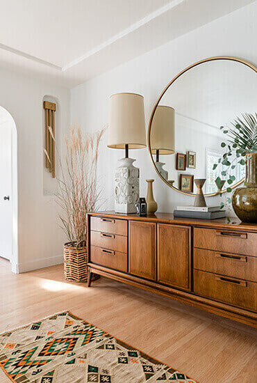 Wood dresser with large round wood mirror and plants surrounding
