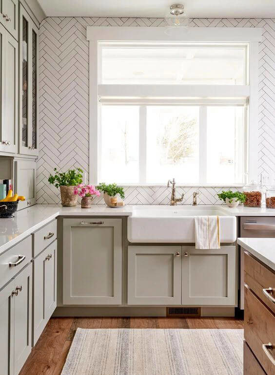 Herringbone backsplash sits over sage green cabinetry and large farmhouse sink