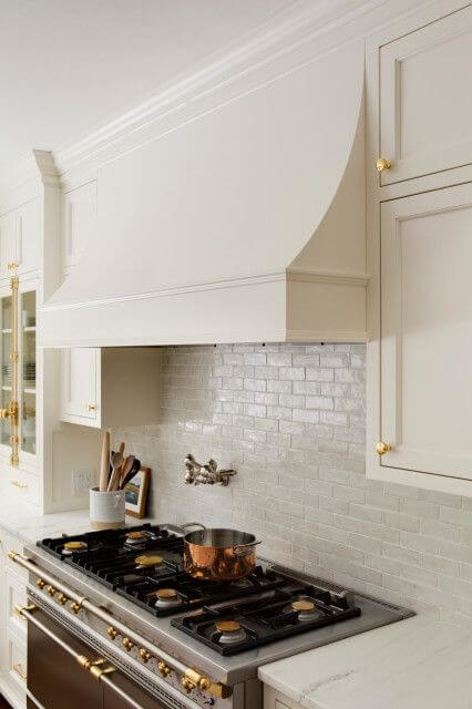 Bright white kitchen with sloped hood fan and gold cabinet hardware