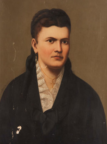 Dated 1877, this mid-Victorian era portrait depicts a somber woman with rich brown hair drawn up in braids, wearing pearl droplets and a simple golden cross around her throat. She is wrapped in a coat of black with a slight ruffle around the collar, yet it is the delicate flurry of lace at her throat that demands the most attention, marking the rise of mass production and accessibility of luxuries such as bolts of lace. Given the plain backdrop and obscure artist’s name, one might be curious if this was a self-portrait, or one done by a dear friend or family member.