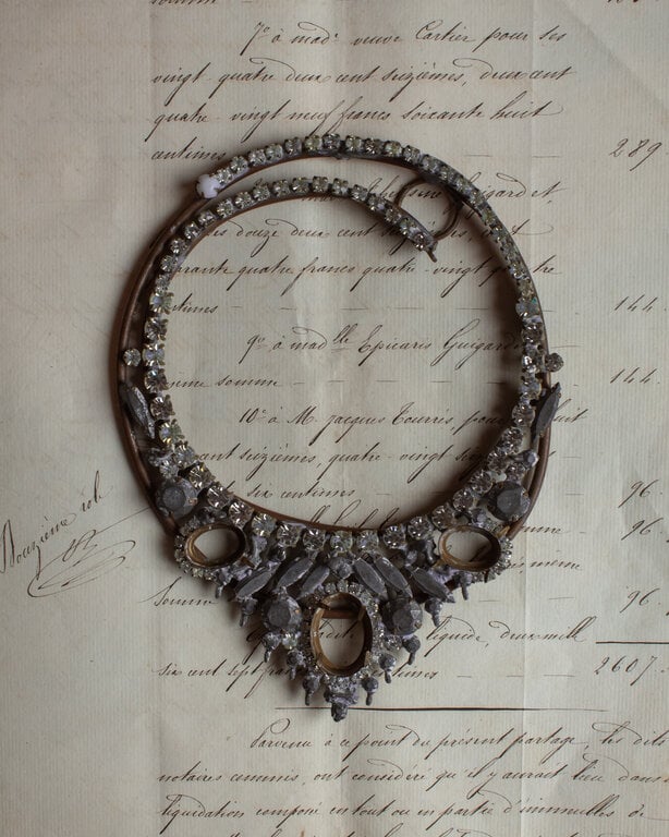A luminous vintage armature necklace featuring clear and pale yellow rhinestones, sculptural leaf-like settings, and open oval frames arranged across aged metalwork. Its intricate, timeworn construction gives it an elegant one-of-a-kind presence.