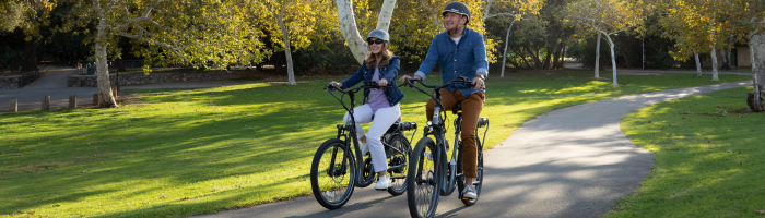 Two people ride Pedego Electric bikes on bike path