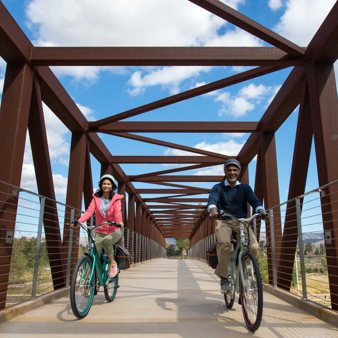Two people ride Pedego Electric Bikes on a bridge