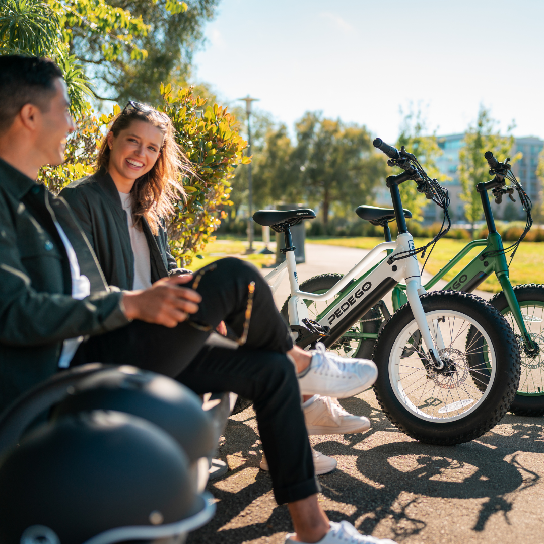 Two people sit on a bench with their Pedego Electric bikes in the background