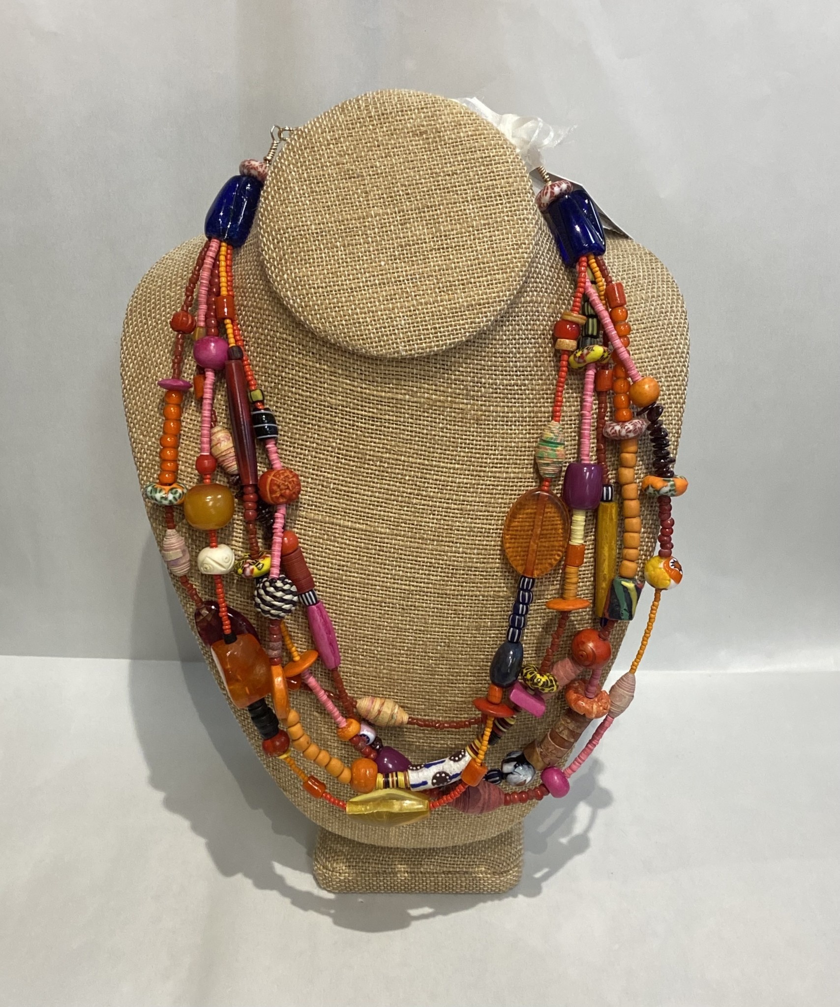 Beverly Creamer BAC13 – Five strand multi-color piece but predominantly in warm peaches, pinks and red, with new African glass trade beads, Murano glass beads, wooden discs and tubes, garnet pebbles, orange white hearts, amber, resin from Paris, woven black and white bea
