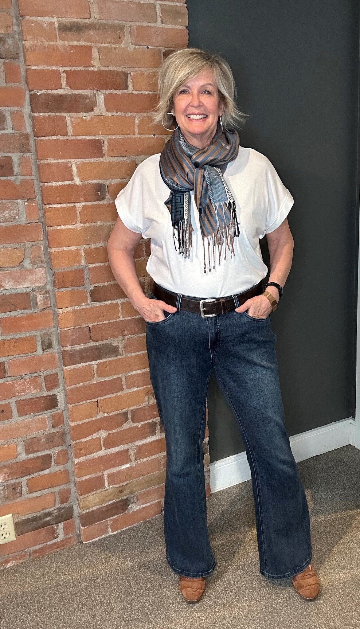 A woman wearing a pair of flared denim jeans, a white t-shirt and a scarf.