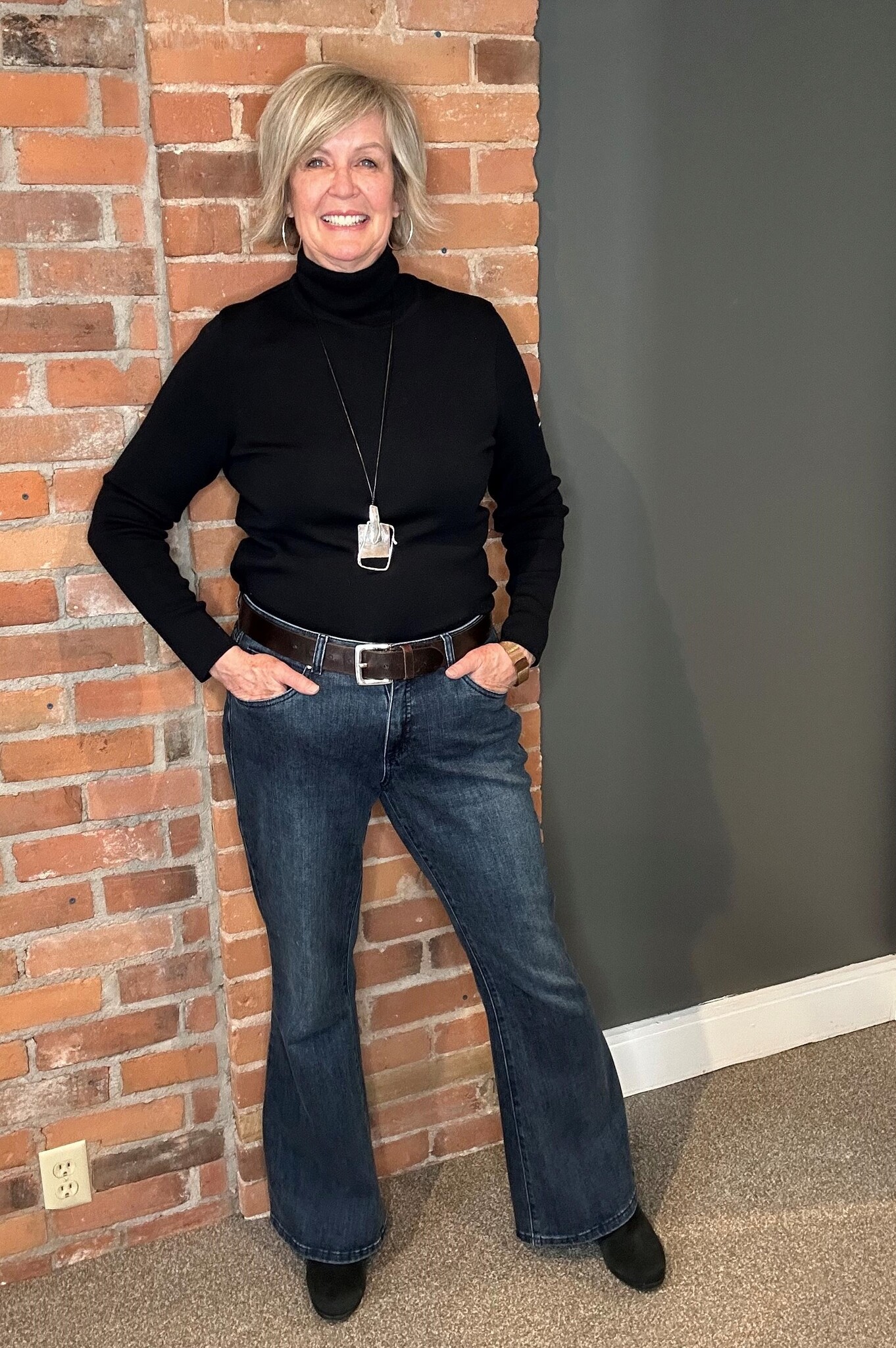 A woman wearing a pair of flared denim pants and a black turtleneck sweater.