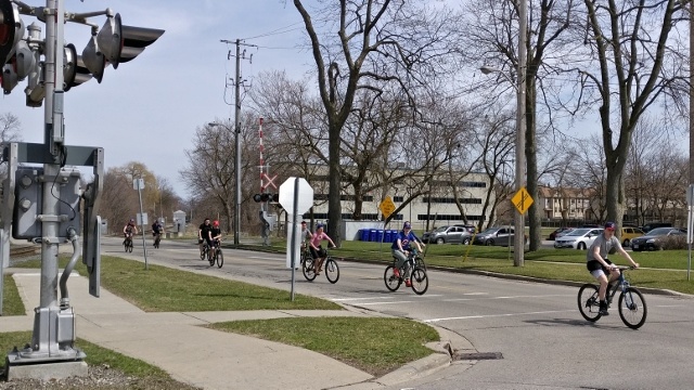 A varied group of cyclists crosses a level train crossing.