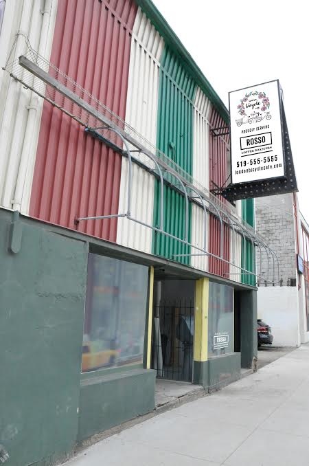 Image of the store front, with red white and green striping on the upper half behind the hanging store sign.