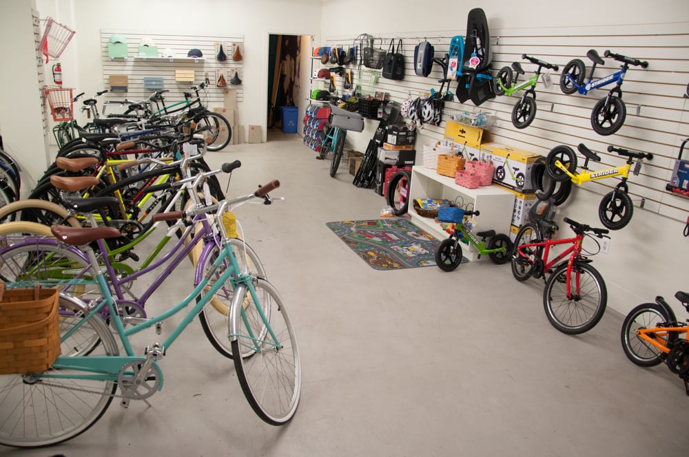 A line up of colorful step through bicycles with some accessories on the walls like bike seats and bags.