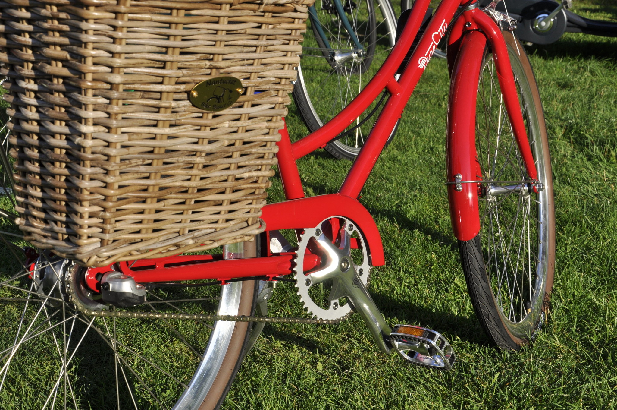 A closeup of a wicker basket on the back of a red step through Pure Cycles bicycle.