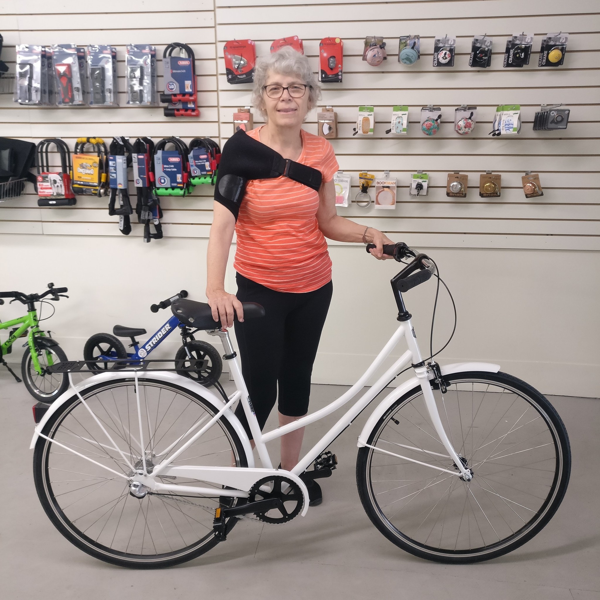 Linda and her bike in front of a retail wall of bicycle bells.