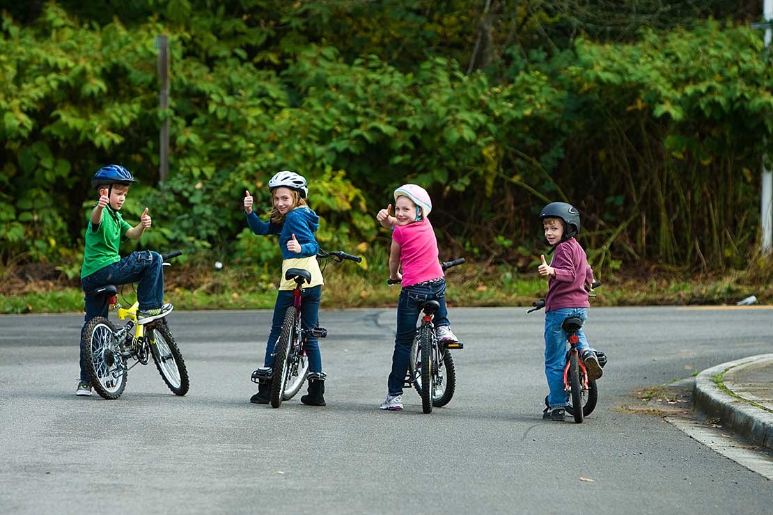 Four kids on bikes look over their shoulders to give a thumbs up to the camera