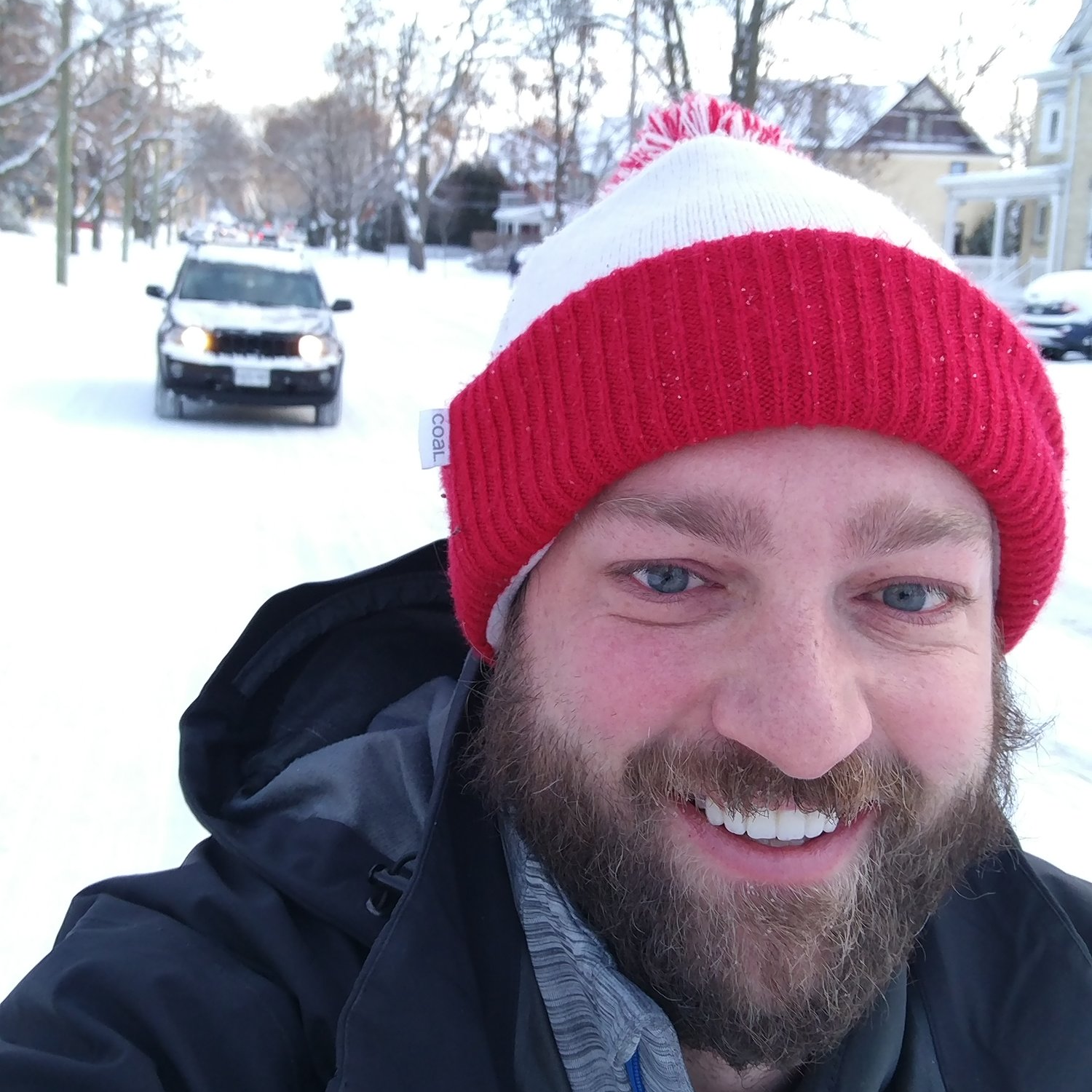 Ben is wearing a toque and smiling as he takes a selfie with a snowy street behind him.