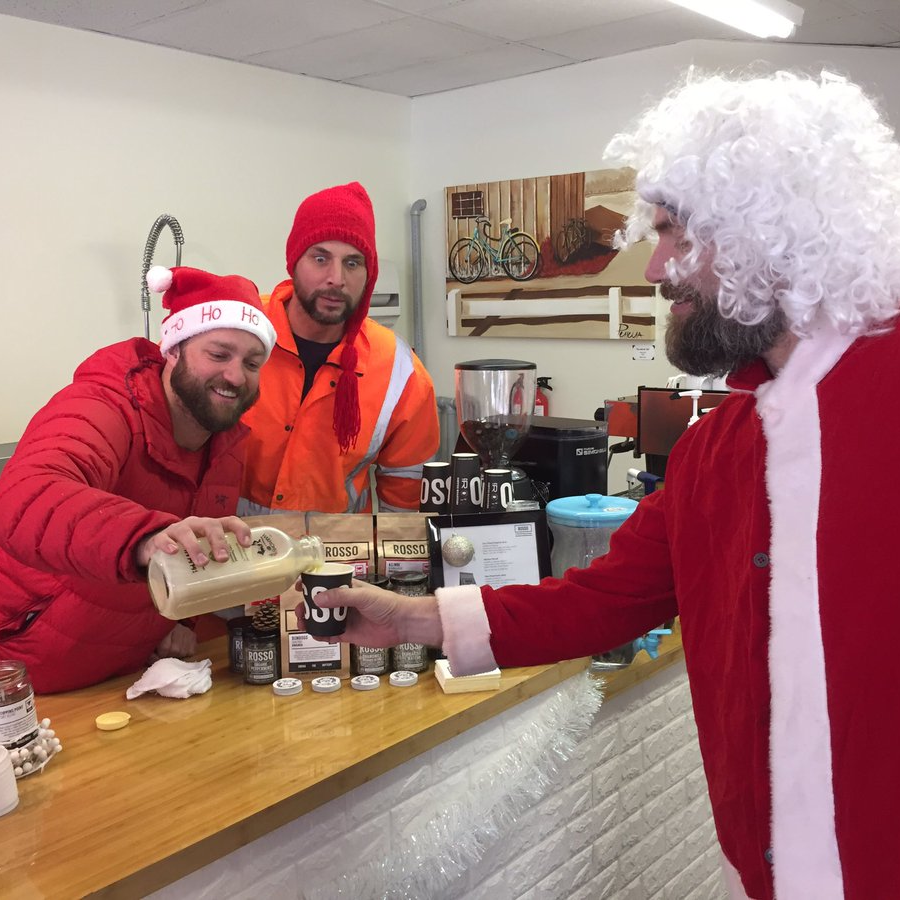 Ben pours a santa a glass of eggnog. A friend looks jealously over his shoulder at the eggnog.