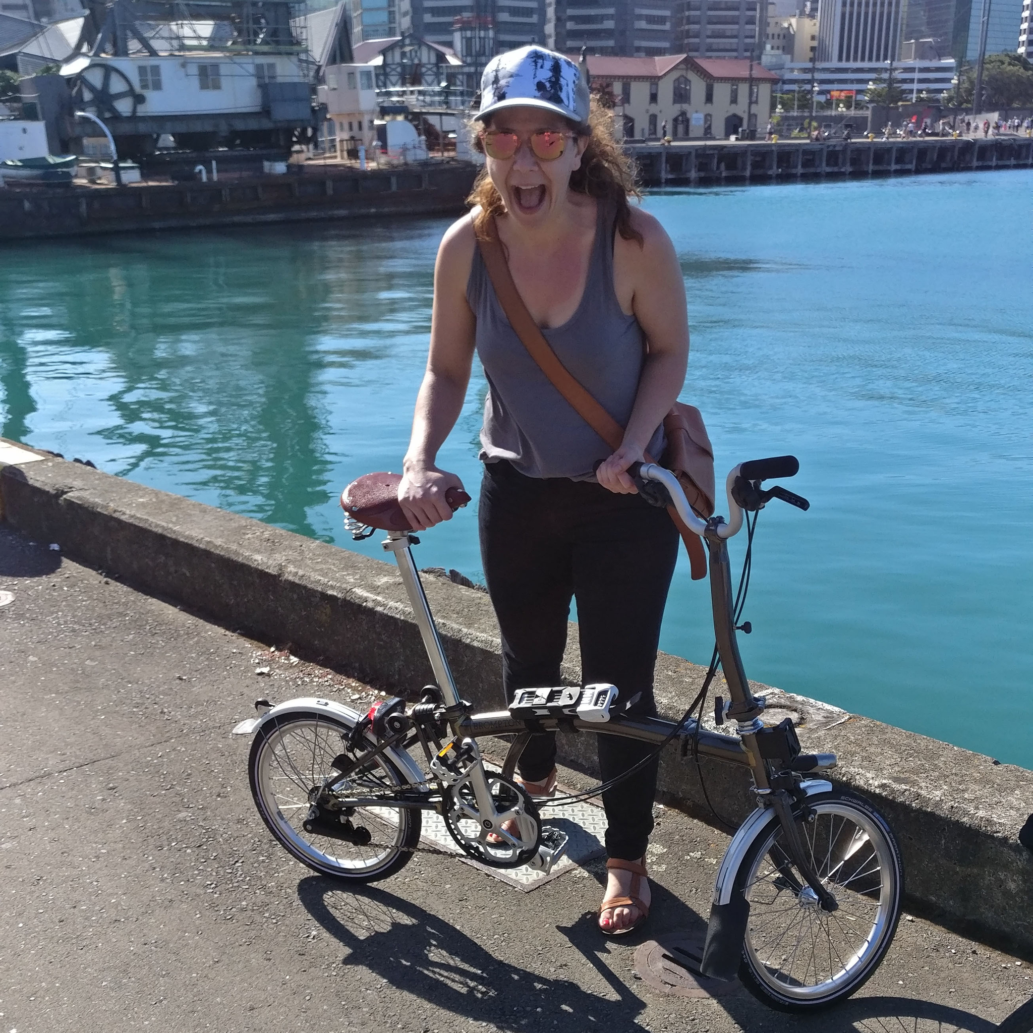 Caroline yells with a smile at the camera while standing behind her Brompton bike.