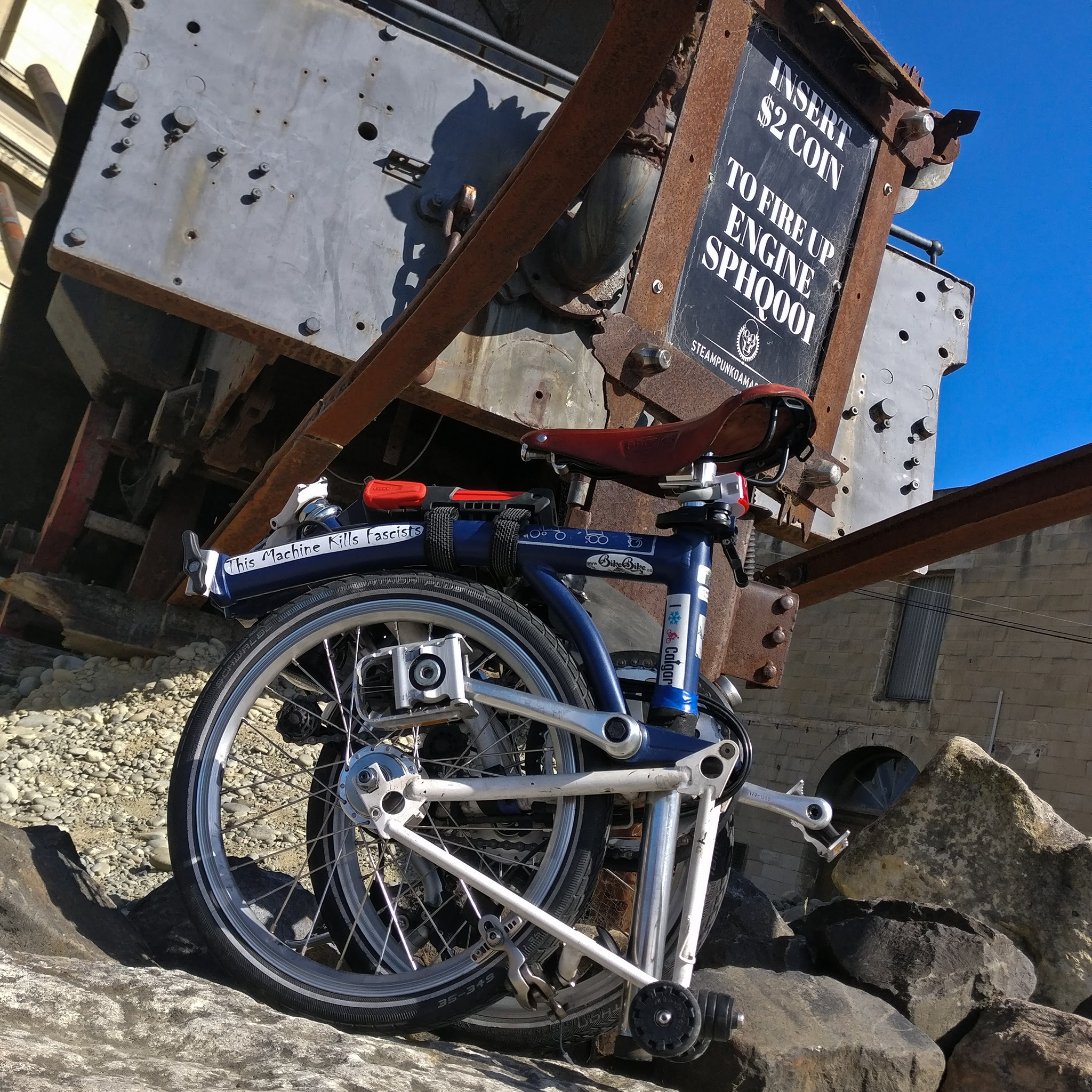 A folded Brompton on a rock beyond which is a sign that says "insert coin to start up engine"