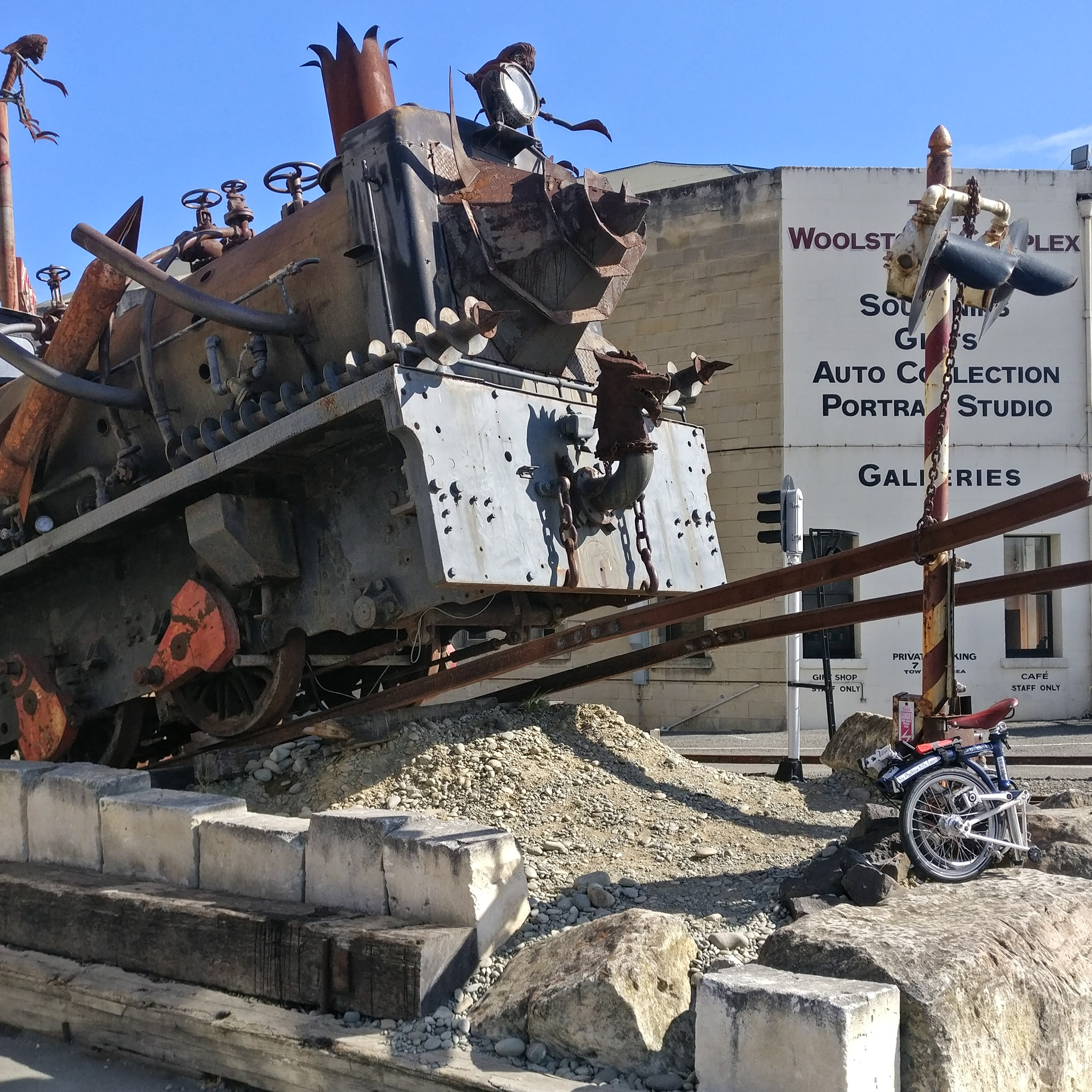 A folded Brompton on a rock in front of a large run down train engine.